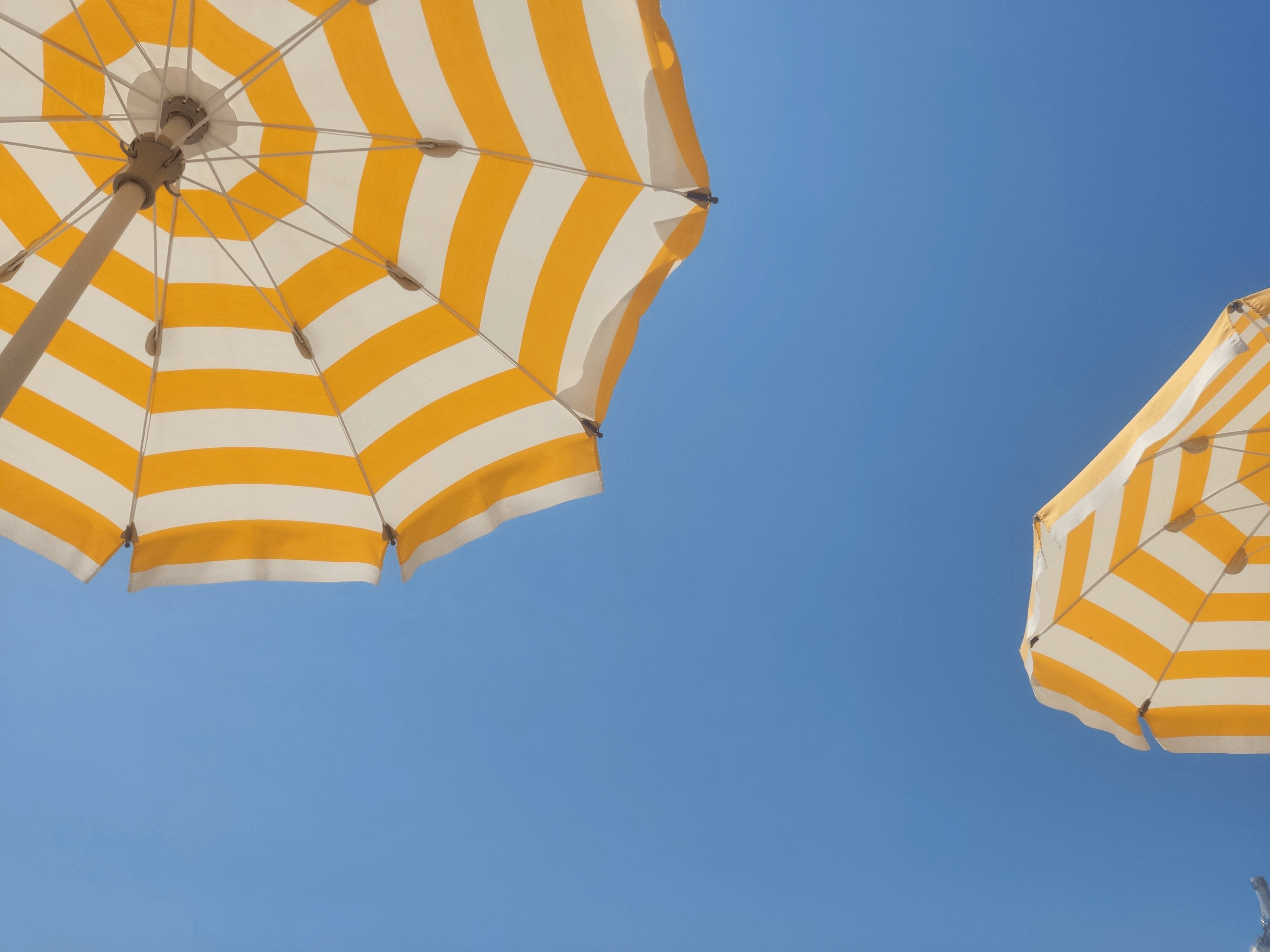 Gelb weiß gestreifter Sonnenschirm vor blauem Himmel. Symbolisiert den UV Filter Tinosorb S.